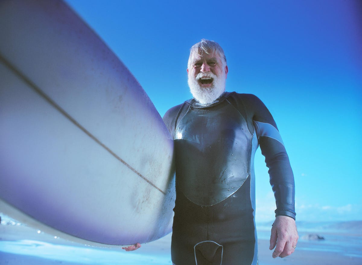 A bearded man holding a surfboard in the water