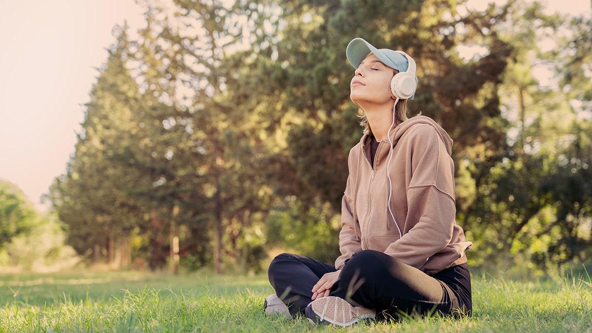 a woman meditates outside wearing headphones