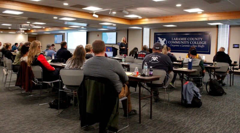 A room full of people looks at a woman speaking at the front of the room